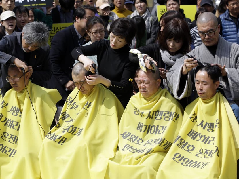 Relatives of victims of the South Korean ferry sinking that killed more than 300 a year ago, have their heads shaved during a rally against the government's plans in Seoul, South Korea, Thursday, April 2, 2015.  Dozens of relatives of victims protested against the government plans to provide about 420 million won (S$522,000) for each of the 250 students on the ship and 760 million won for 11 dead teachers. The letters on yellow apron read "Intactly salvage the ferry Sewol and Abrogate the government's plan." Photo: AP