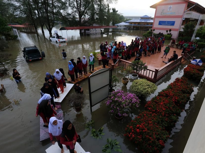 Students crossing a rudimentary “bridge” made of tables to reach their school. Hundreds of students in Penang brave the flood waters on Monday morning (Nov 6) to sit for the Sijil Pelajaran Malaysia (Malaysian Certificate of Education or SPM) examination. Photo: Malay Mail Online.
