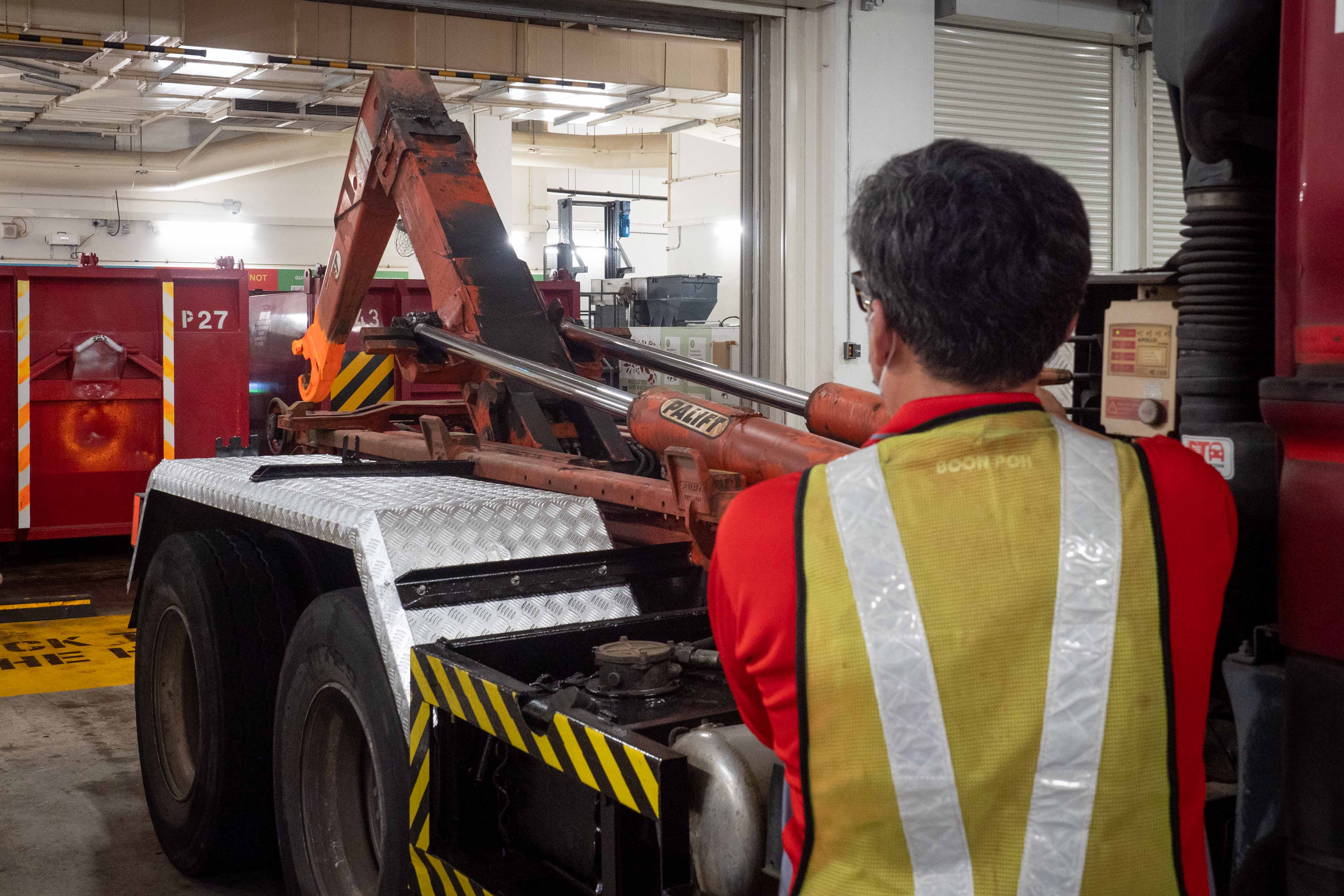 A worker in the waste management sector using an automated arm of the truck to load compacted trash.