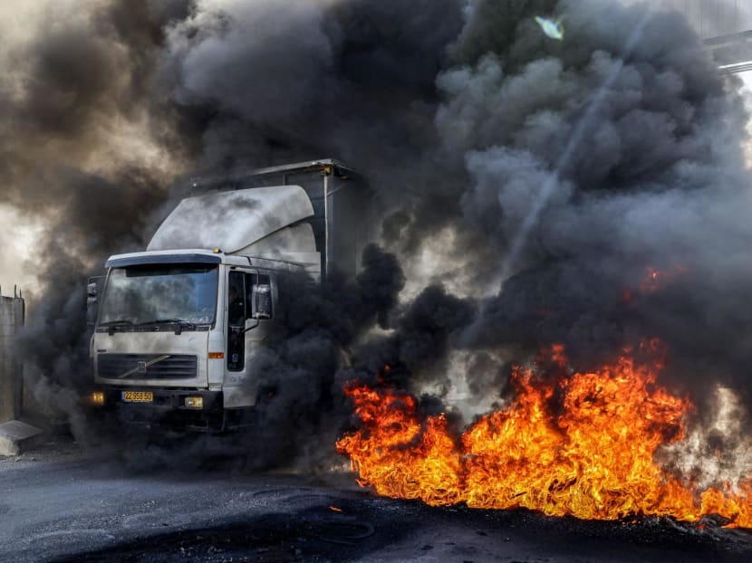 A truck headed towards Nablus drives past burning tires at the Hawara checkpoint south of the Palestinian city in the occupied West Bank on Nov 1, 2022, which were set aflame by Palestinian protesters demanding the reopening of roads around the closed-off city of Nablus, which has been under military lockdown since Oct 11 after Palestinian gunmen kiled an Israeli soldier near the settlement of Shavei Shomron.