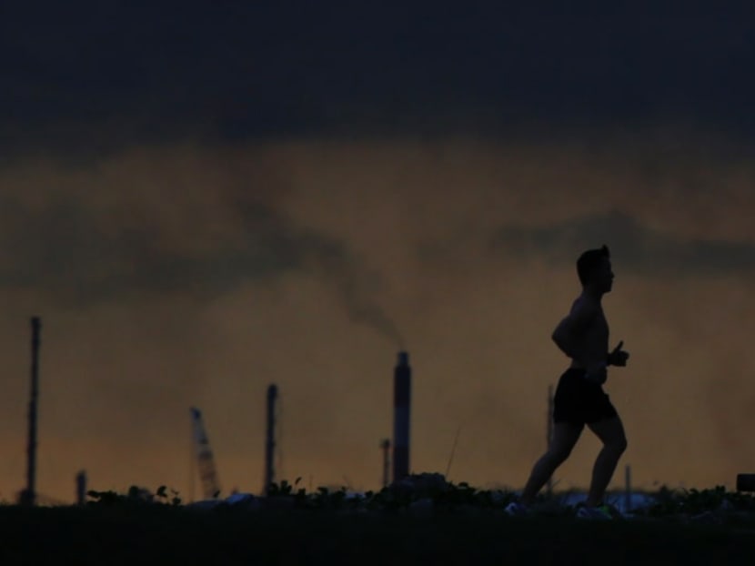 A man running past a chimney giving off emissions in an industrial area of Singapore.