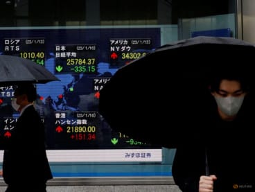 FILE PHOTO: Men walk past an electric board displaying Nikkei and other countries' indexes outside a brokerage in Tokyo, Japan January 16, 2023.  REUTERS/Kim Kyung-Hoon