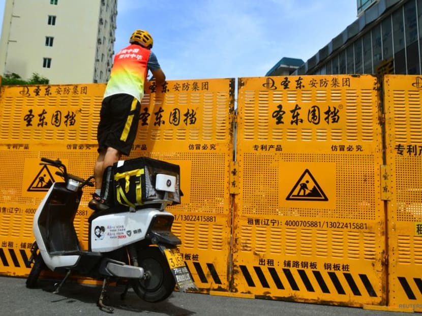 A courier stands on an electric bike to make a delivery over a barricade, amid lockdown measures to curb the coronavirus disease (Covid-19) outbreak in Sanya, Hainan province, China August 6, 2022. China Daily via REUTERS A courier stands on an electric bike to make a delivery over a barricade, amid lockdown measures to curb the coronavirus disease (Covid-19) outbreak in Sanya, Hainan province, China August 6, 2022. China Daily via REUTERS