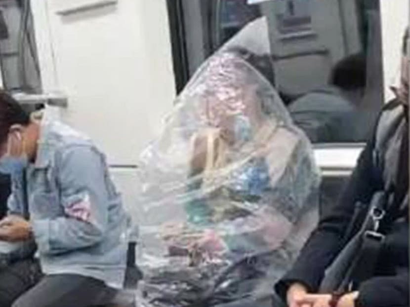 Screenshot from a video showing a woman in Wuhan, China in a subway train covering herself with a huge plastic bag to eat a banana.