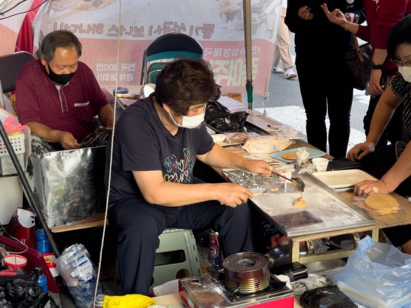 In this picture taken in Seoul on Oct 10, 2021, customers wait in line as street vendor Jung Jung-soon and her husband Lim Chang-joo sell freshly made dalgonas, a crisp sugar candy featured in the Netflix smash hit series Squid Game, for which they were hired to be on set to make during production. In this picture taken in Seoul on Oct 10, 2021, customers wait in line as street vendor Jung Jung-soon and her husband Lim Chang-joo sell freshly made dalgonas, a crisp sugar candy featured in the Netflix smash hit series Squid Game, for which they were hired to be on set to make during production.