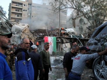 People gather near a damaged site, hauling a destroyed vehicle away, after what Syrian and Iranian media described as an Israeli air strike on Iran's consulate in the Syrian capital Damascus, on April 1, 2024.