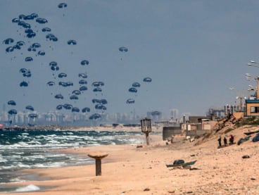 Humanitarian aid is dropped on the Gaza Strip, west of Gaza City, on March 25, 2024 amid the ongoing conflict in the Palestinian territory between Israel and the militant group Hamas, with the background showing Israel's Rutenberg power station near Ashkelon.