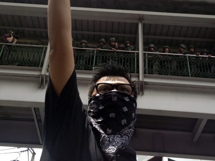 An anti-coup protester gives a three-finger salute, inspired by The Hunger Games movie, as soldiers keep eyes on him from an elevated walkway near a rally site in central Bangkok, Thailand. Photo: AP