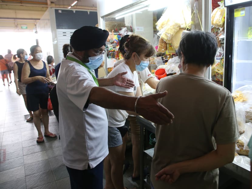 A National Environment Agency safe distancing ambassador reminding patrons to keep a safe distance from each other at a stall during an enforcement operation at Chong Boon Market on April 10, 2020.