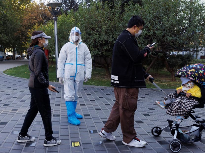 A pandemic prevention worker wears a protective suit as people line up to get swab tests at a testing booth as outbreaks of Covid-19 continue in Beijing, China on Nov 3, 2022. 