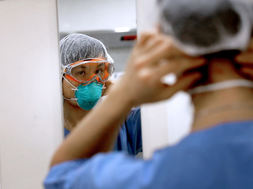 Ms Ong Zh Hua, an assistant nurse clinician at Tan Tock Seng Hospital who works in both the screening centre and emergency department, checks herself in the mirror as she dons a full set of personal protective equipment.