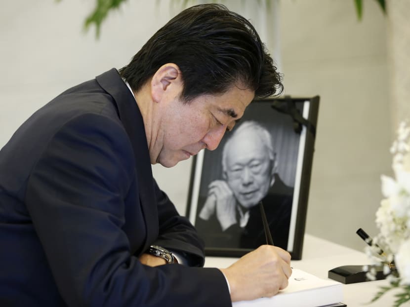Japan's Prime Minister Shinzo Abe signs a condolences book for the late Lee Kuan Yew in front of a memorial photo of Lee at the Singapore Embasssy in Tokyo, March 24, 2015. Photo: Reuters