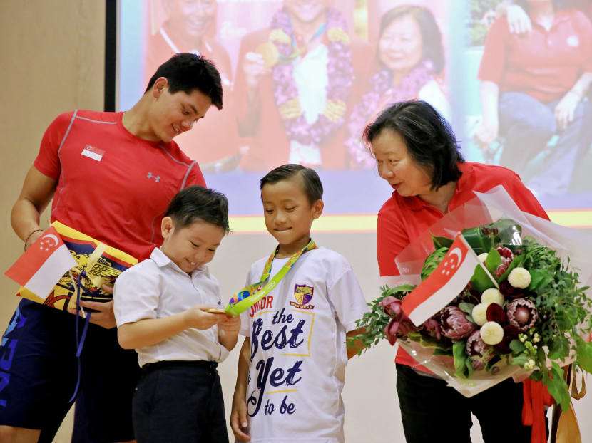 (2nd from left) Darion Pang Jun Jia, 9, Primary 3, looking at the gold medal that Marcus Lim, 10, Primary 4, wearing on while Joseph Isaac Schooling and his mother May Schooling look on. Photo: Koh Mui Fong