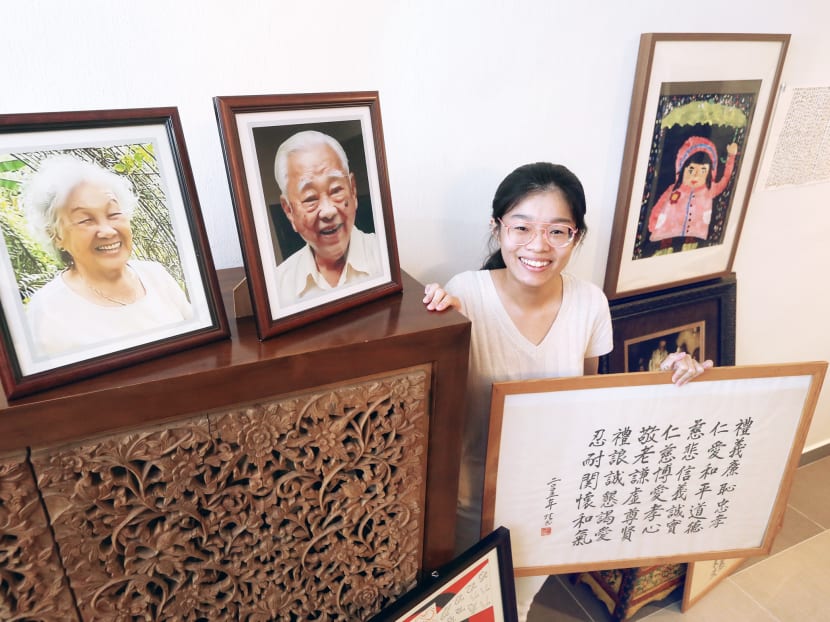 The author is pictured here with photos of her late grandparents and a calligraphy done by her grandfather.