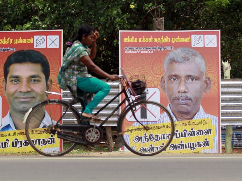 A Sri Lankan ethnic Tamil woman pedals past posters of Sri Lanka's ruling United People's Freedom Front. Photo: AP