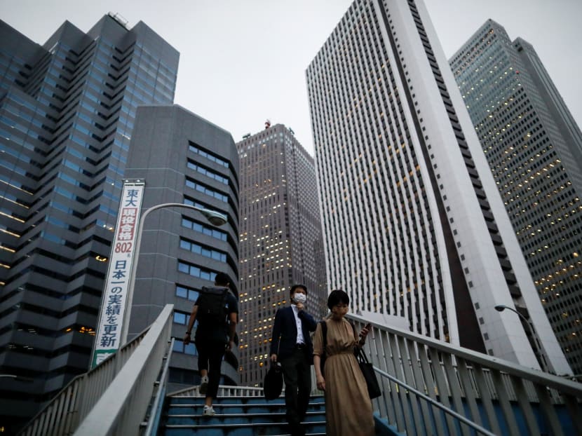 People wearing protective face masks walk down stairs in front of office buildings in Tokyo's Shinjuku district, June 24, 2020.