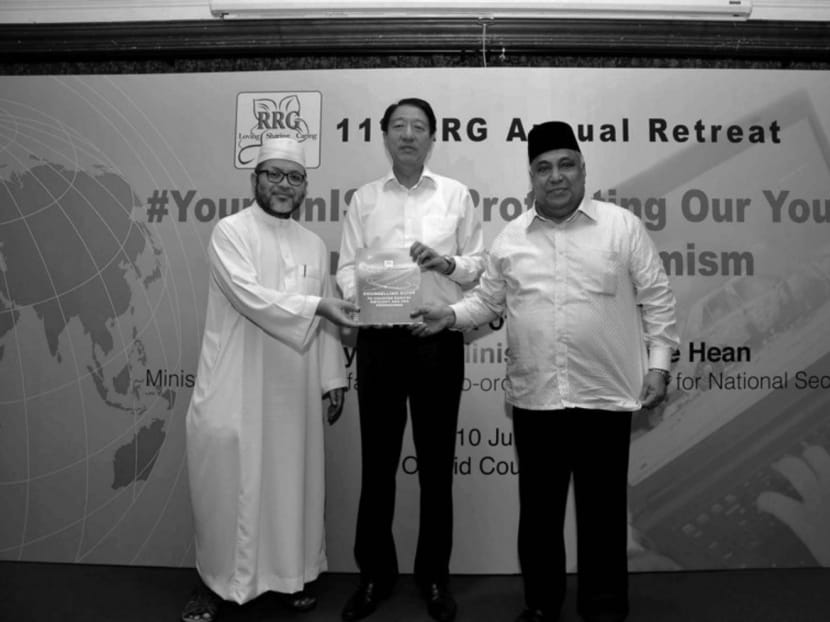 DPM Teo Chee Hean, Ustaz Mohamad Hasbi Hassan (left) and Ustaz Ali Haji Mohamed (right) with a manual for RRG counsellors on refuting ISIS ideology. Photo: Ministry of Home Affairs