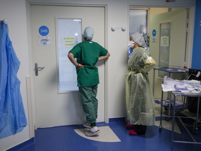 Nurses look through a glass door at a patient infected with Covid-19 as they lie in an intensive care room of The Estree Private Hospital at Stains on the outskirts of Paris on Nov 12, 2020.