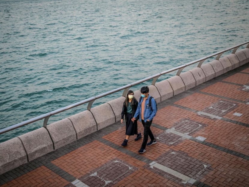 A couple wearing masks hold hands while walking along the waterfront in Hong Kong on February 22, 2020.