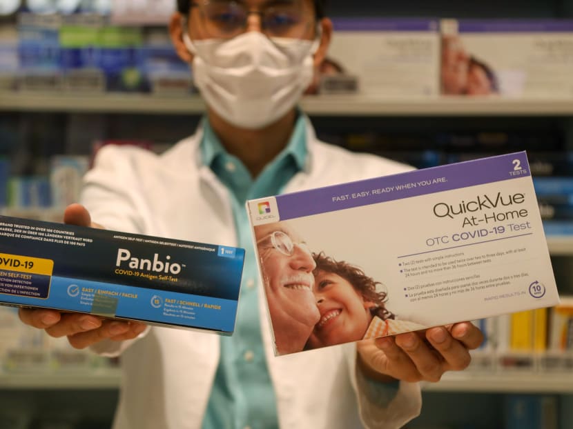 A pharmacist at Unity Pharmacy in VivoCity mall holding up the Abbott Panbio and Quidel QuickVue ART kits on June 16, 2021.
