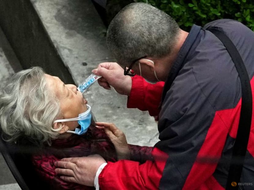 FILE PHOTO: A man helps a woman to consume a packet of traditional Chinese medicine (TCM) Lianhua Qingwen, as she sits by the side of a road outside a residential compound, during a lockdown to curb the spread of the coronavirus disease (COVID-19) in Shanghai, China April 5, 2022. REUTERS/Aly Song