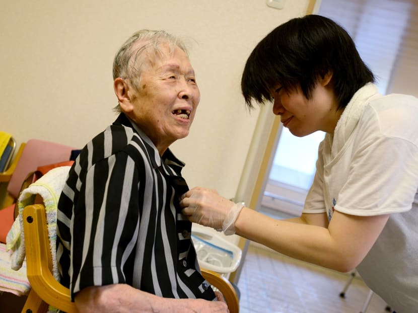 A care worker, right, helps Asayo Sakai, a former nurse and housewife who was diagnosed with Alzheimer's disease almost 10 years ago, dress after taking a bath at the Soyokaze day service in Osaka on Thursday, Aug. 6, 2014. While other countries are aging, none have done so as rapidly as Japan, where an estimated 8 million people suffer from dementia or show early signs of developing the disease. Source: Bloomberg