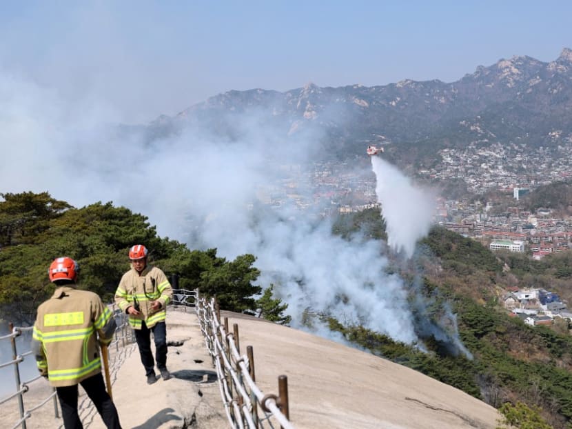 This picture taken on April 2, 2023 shows firefighters watching as a helicopter douses a wildfire on Mount Inwang in Seoul.