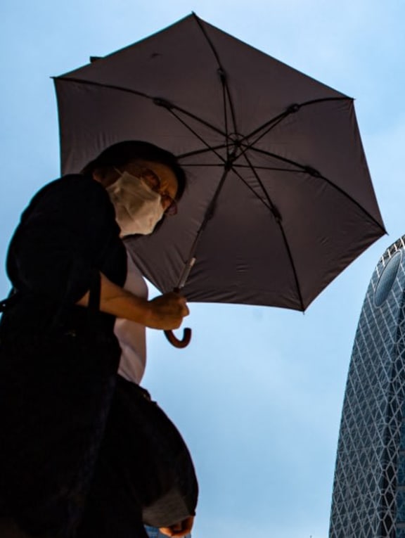 A pedestrian walking with an umbrella to shield from the sun in the midst of a heatwave in Tokyo's Shinjuku district in June 2022.