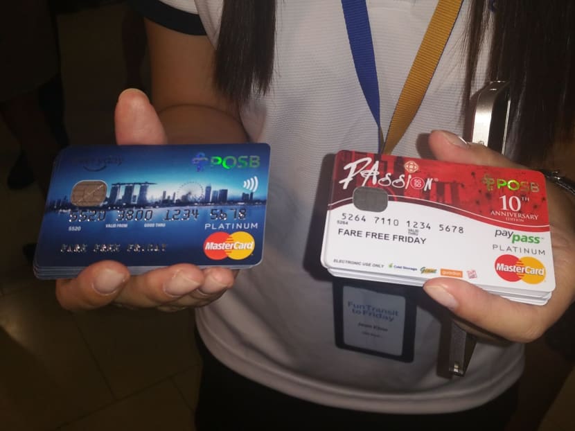 A POSB employee holding up POSB Everyday Credit Cards and PAssion POSB Debit Cards that cardholders can use to enjoy unlimited free MRT, LRT and bus rides every Friday till the end of this year. Photo: Amanda Lee