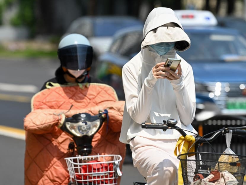A woman wearing sun protective clothing commutes on a bicycle amid hot weather in Shanghai on May 29, 2023. 