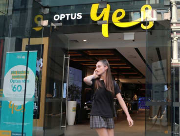 FILE PHOTO: A woman uses her mobile phone as she walks past in front of an Optus shop in Sydney, Australia, February 8, 2018. REUTERS/Daniel Munoz/File Photo