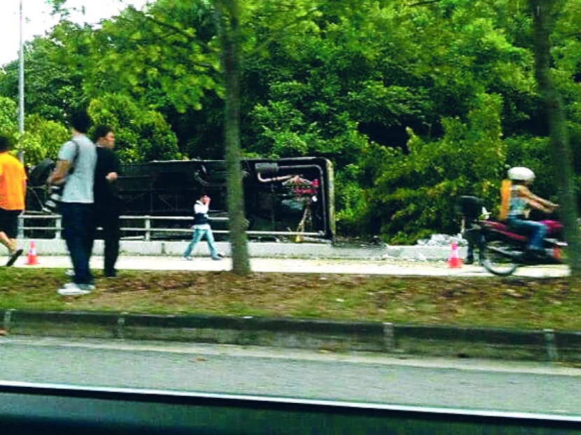 The bus veered across the road to the centre divider and hit the concrete barrier before toppling over. Photo: Channel NewsAsia