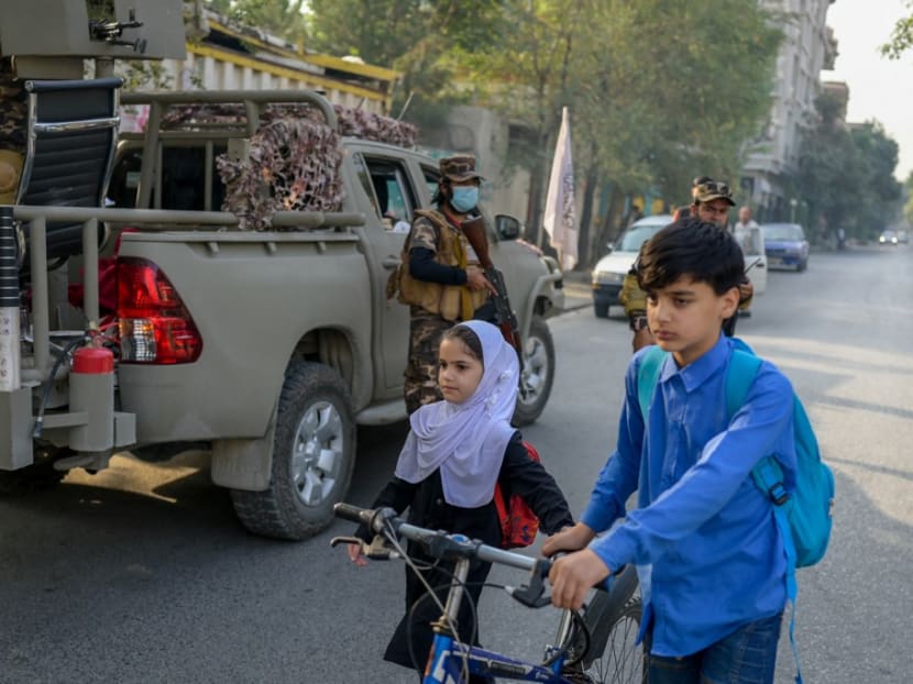 School children walk past Taliban special forces' personnel deployed along a road near the venue of a demonstration by women protestors outside a school in Kabul on Sept 30, 2021.