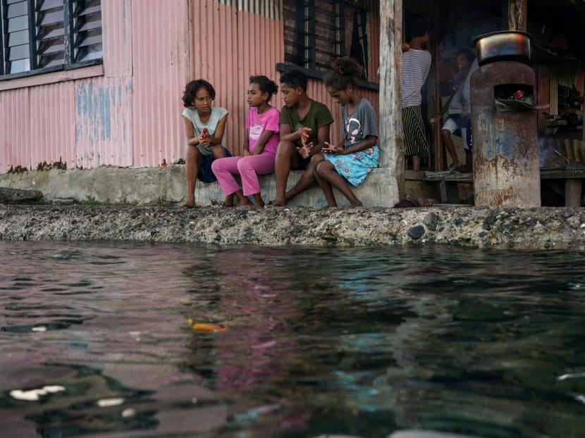Children from a village in Fiji sitting outside their home next to a flooding sea wall at high tide. Children from a village in Fiji sitting outside their home next to a flooding sea wall at high tide.