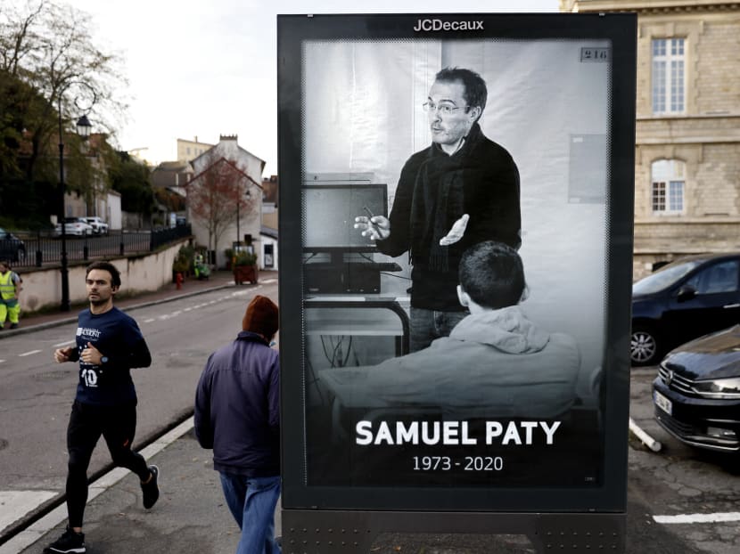 Pedestrians pass by a poster depicting French teacher Samuel Paty placed in the city center of Conflans-Sainte-Honorine, 30km northwest of Paris on Nov 3, 2020, following the decapitation of the teacher on Oct 16, 2020.