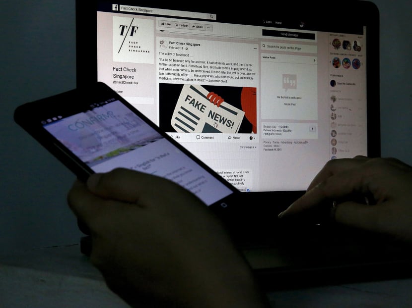 Close-up of a lady reading the Fact Check Singapore facebook page while holding a mobile phone with the Confirm? website in the background. Photo illustration: Koh Mui Fong/TODAY