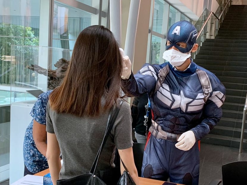 A staff member of NUS Business School manning the temperature screening station dons a Captain America costume to bring some cheer to those in line. The author says employees who help others are likely to improve their psychological wellbeing.