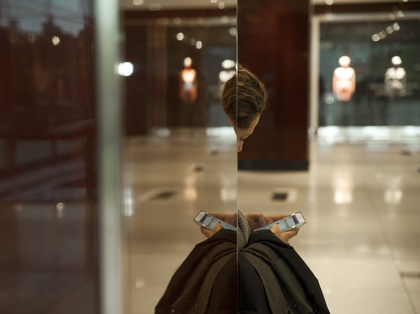 Seen in partial reflection, a woman checks a Facebook app in the Time Warner Centre lobby, in Manhattan on Oct 27, 2016. Photo: The New York Times