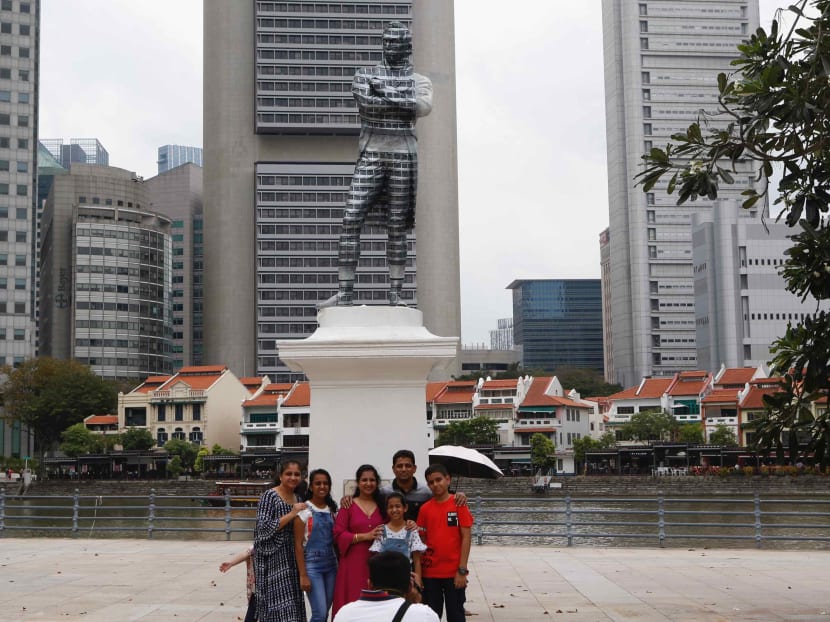 People posing in front of an optical illusion involving the statue of Sir Stamford Raffles. The author notes that there is a wide range of colonial experiences across the world, and in some cases, Western colonisation have left a positive legacy.