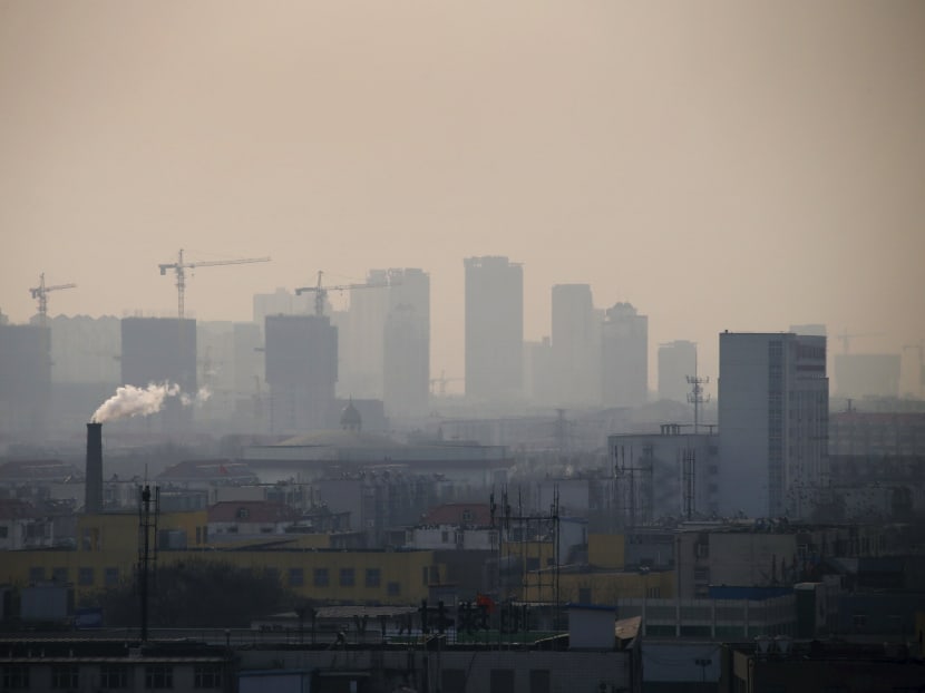 Smoke rises from a chimney among houses as new high-rise residential buildings are seen under construction on a hazy day in the city centre of Tangshan, Hebei province. Photo: Reuters