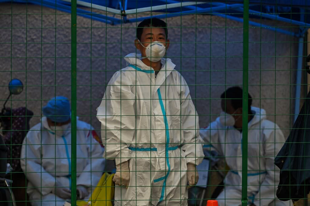 A worker wearing personal protective equipment stands behind a fence in a residential area under Covid-19 lockdown in the Huangpu district of Shanghai on June 13, 2022.