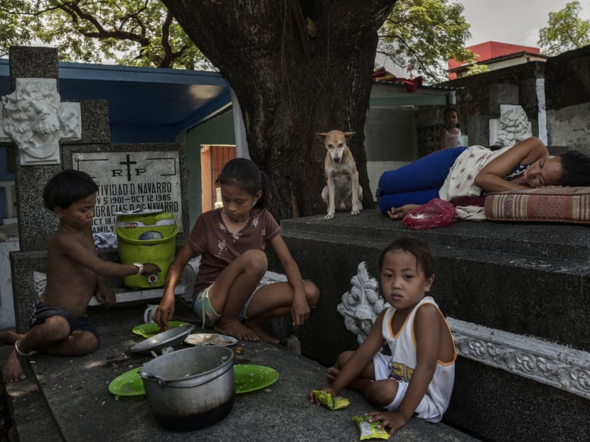 A family having  lunch on the tombs where they live in Manila North Cemetery.The cemetery is inhabited by some of Manila’s poorest people, living in the crypts and mausoleums of wealthy families who pay them a stipend to clean and watch over them. PHOTO: The New York Times