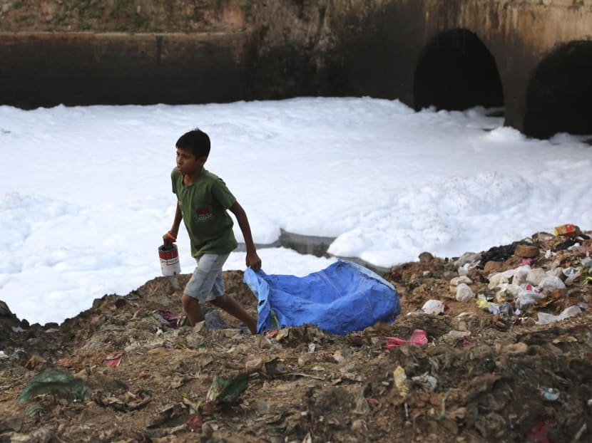 A young garbage collector looks for valuables in the garbage dumped on the banks of Bellundur Lake, which is filled with froth from industrial pollution in Bangalore, India, May 25, 2015.  Photo: AP