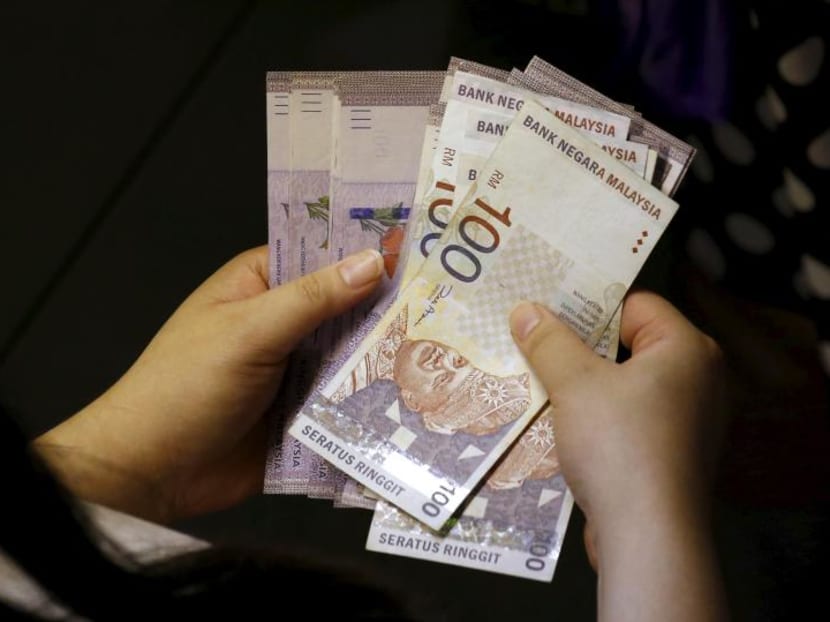 A customer counts her ringgit notes outside a money changer at the central business district in Singapore.