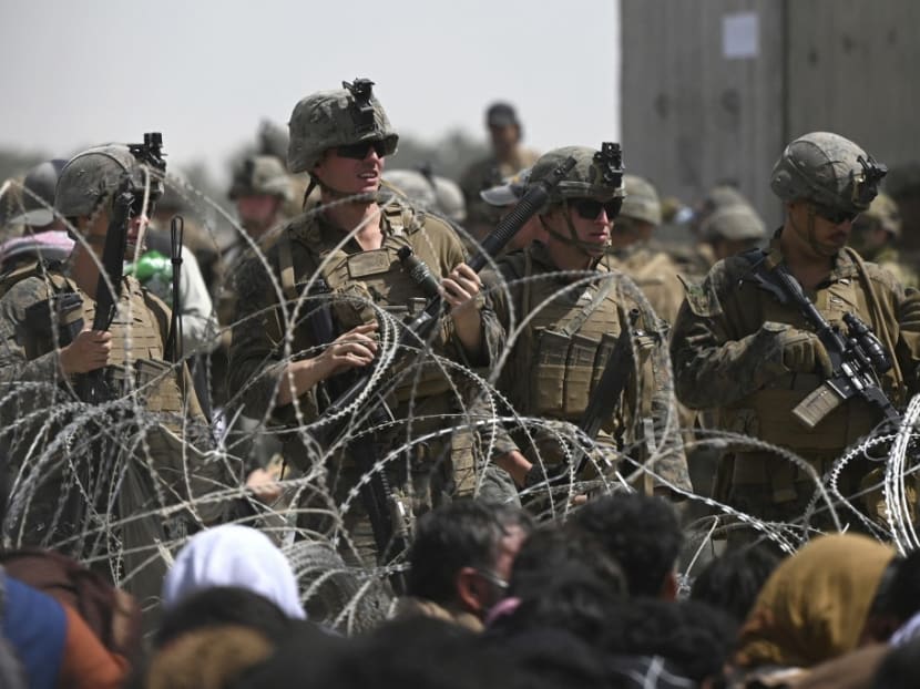 US soldiers stand guard behind barbed wire as Afghans sit on a roadside near the military part of the airport in Kabul on August 20, 2021, hoping to flee from the country after the Taliban's military takeover of Afghanistan.