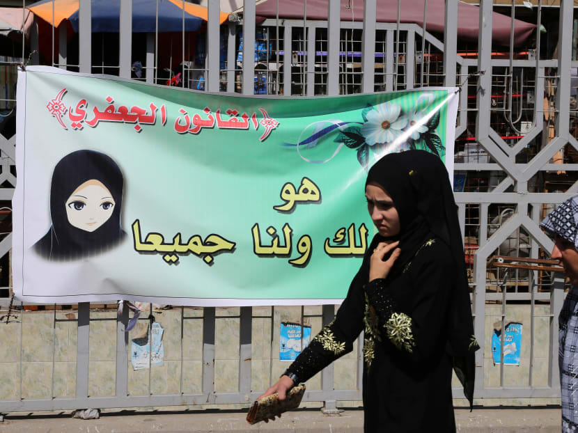Women pass by a banner for the Jaafari Personal Status Law in Baghdad, Iraq. The Arabic on the banner reads, "The Jaafari Personal Status Law is for you and all of us." Photo: AP