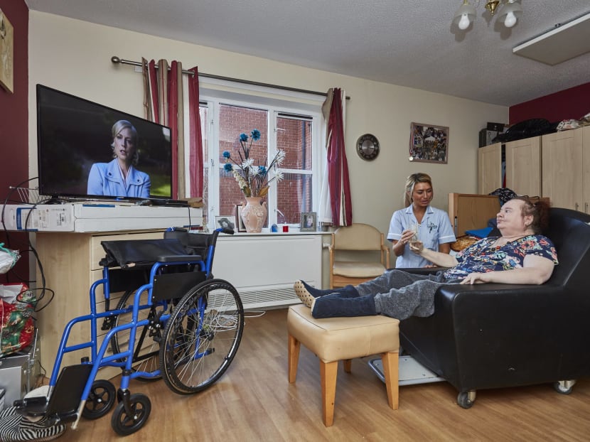 A patient and caretaker in a room at the Millbrow Care Home in Widnes, England. Revelations of poor conditions at Millbrow under its private provider reflect broader concerns about the nation’s outsourcing practices. Photo: The New York Times