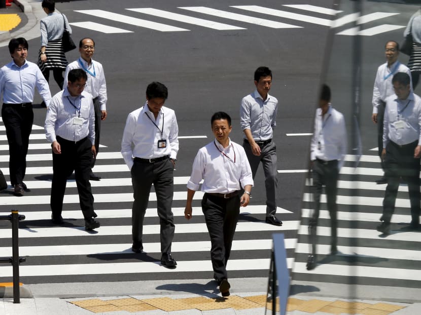 Office workers are reflected in a glass railing as they cross a street during lunch hour in Tokyo June 1, 2015. Photo: Reuters