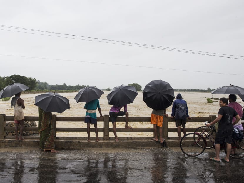 Nepali girl shelters under a umbrella during heavy rains while crossing a flooded water at Saptari distric, some 300km from Kathmandu on August 12, 2017. Floods and landslides caused by torrential monsoon rains have killed at least 25 people in the last two days across Nepal, officials said on August 12. Photo: AFP