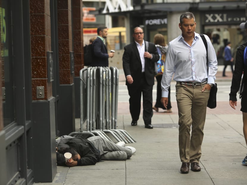 Pedestrians pass a man laying on the sidewalk near the Powell Street Bay Area Rapid Transit and MUNI public transportation system station in San Francisco, California, July 23, 2014.  Photo: Reuters